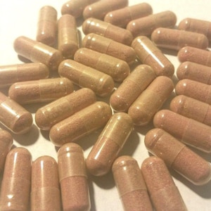 May include: A large group of brown capsules, likely a dietary supplement, are scattered on a white surface.
