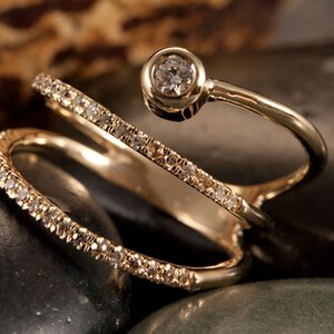 May include: A gold ring with three bands, each set with small diamonds. The top band has a larger diamond in a bezel setting.
