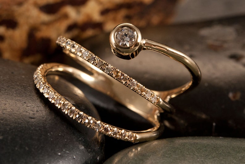 May include: A gold ring with three bands, each set with small diamonds. The top band has a larger diamond in a bezel setting.