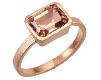 May include: A rose gold ring with a rectangular, light brown gemstone set in a bezel setting.