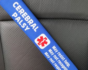 May include: A blue seatbelt cover with the words "CEREBRAL PALSY" in white. It includes a red medical symbol and text that reads "May resist help. May not recognize danger. May not respond."