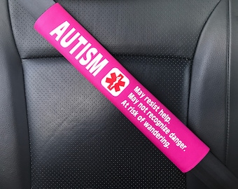 May include: Pink car seat belt cover with the word "AUTISM" and a medical symbol. The text reads "May resist help. May not recognize danger. At risk of wandering."