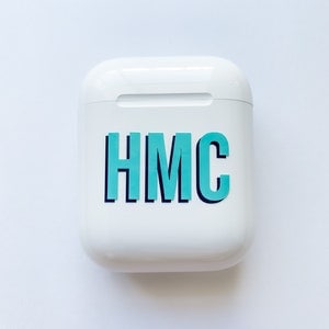 May include: White wireless charging case with a teal blue sticker that says "HMC" on it.