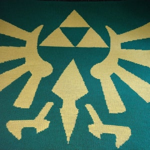 May include: A handmade, knitted blanket featuring the iconic Triforce symbol from the Legend of Zelda video game series. The blanket has a teal background with a light yellow Triforce design. The design includes a triangle and stylized shapes.