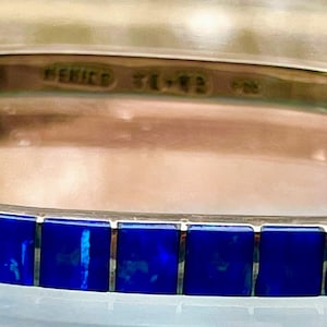 May include: Silver bangle bracelet with a row of square, deep blue inlays. The bracelet is marked "MEXICO TE-43 925". The bracelet has a polished finish and a classic design, suitable for everyday wear or special occasions.