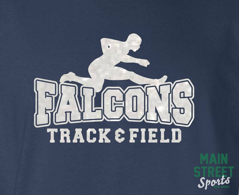 Op de afbeelding: Een marineblauw T-shirt met een wit silhouet van een hardloper die over een horde springt. De tekst "Falcons Track & Field" is in wit onder de hardloper gedrukt. De tekst "Main Street Sports" is in groen in de rechterbenedenhoek van het T-shirt gedrukt.