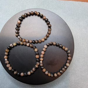 May include: Three black and brown beaded bracelets with silver accents on a black circular surface.