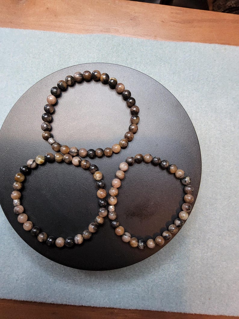 May include: Three black and brown beaded bracelets with silver accents on a black circular surface.