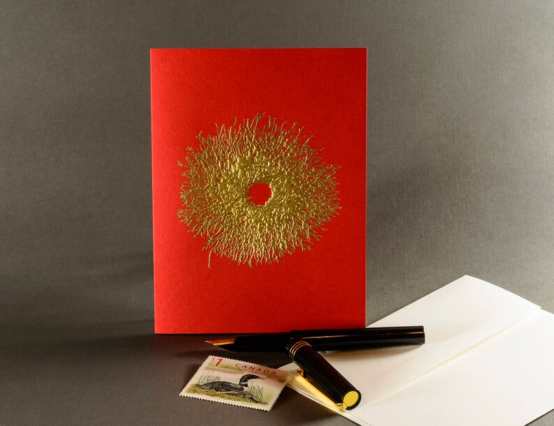 Puede incluir: Una tarjeta roja con un dise&ntilde;o de corona en l&aacute;mina dorada. La tarjeta est&aacute; sobre un sobre blanco con un bol&iacute;grafo negro y un sello con un pato.