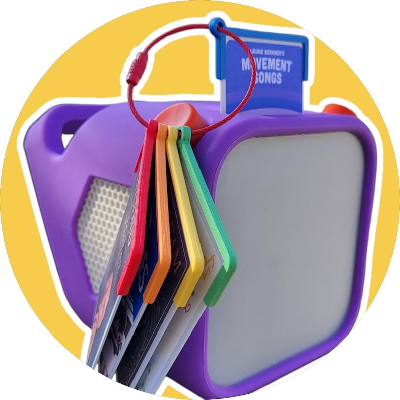 May include: Purple and white television-shaped speaker with a rainbow of colorful keychains attached. The keychain tag reads "Laurie Berkner's Movement Songs".
