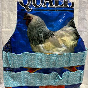 May include: A blue and white apron with a chicken image and the word "QUALITY" printed on it. The apron has two rows of blue fabric pockets with white snowflake patterns.
