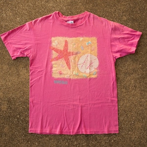 Peut inclure: T-shirt rose avec un motif d'étoile de mer et d'une coquille sur une plage avec le texte "Summer Sun".