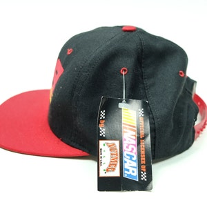 Peut inclure: Casquette de baseball noire et rouge avec un logo NASCAR sur le devant. La casquette a une visi&egrave;re rouge et une couronne noire. La casquette est neuve et a une &eacute;tiquette attach&eacute;e.