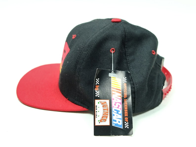 Peut inclure: Casquette de baseball noire et rouge avec un logo NASCAR sur le devant. La casquette a une visi&egrave;re rouge et une couronne noire. La casquette est neuve et a une &eacute;tiquette attach&eacute;e.