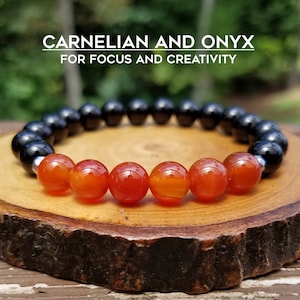 May include: A bracelet made with carnelian and onyx beads. The bracelet is on a wooden surface. The text "CARNELIAN AND ONYX FOR FOCUS AND CREATIVITY" is above the bracelet. The text "ROCK MY ZEN" is below the bracelet.
