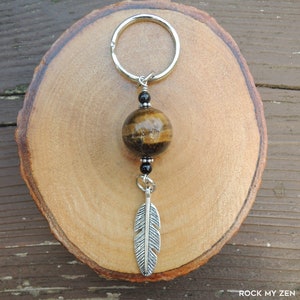 May include: A silver key chain with a brown and gold tiger's eye bead, black beads, and a silver feather charm.