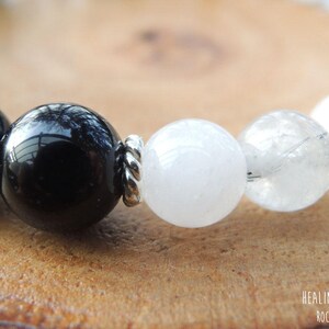 May include: Close-up of a beaded bracelet featuring large, polished black and white gemstone beads. The beads are strung together with silver-colored metal spacers. The bracelet is displayed on a wooden surface.