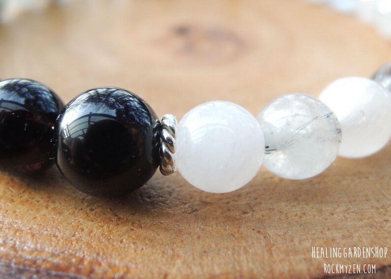 May include: Close-up of a beaded bracelet featuring large, polished black and white gemstone beads. The beads are strung together with silver-colored metal spacers. The bracelet is displayed on a wooden surface.