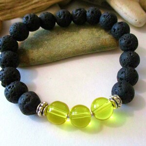 May include: A black lava stone bracelet with three translucent yellow-green beads. The bracelet features round, porous black beads and is accented with silver-colored spacers. The beads are strung on an elastic cord, creating a stretchable design.