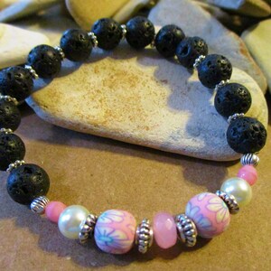 May include: A black lava rock beaded bracelet with pink and white floral beads and silver accents.