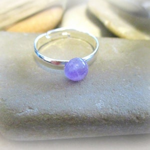May include: A silver adjustable ring with a small, round, light purple amethyst gemstone.