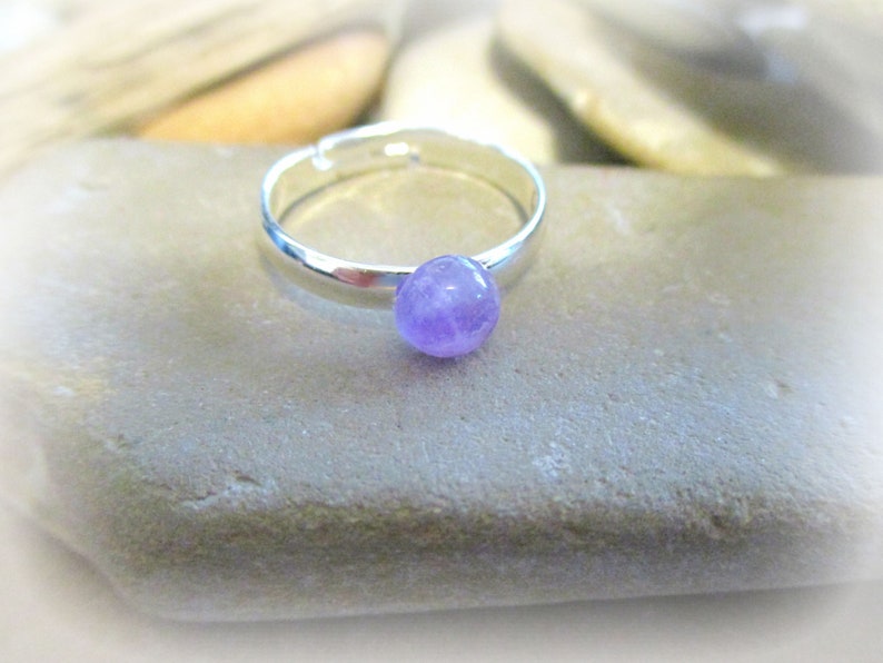 May include: A silver adjustable ring with a small, round, light purple amethyst gemstone.