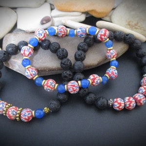 May include: Two bracelets made with black lava rock beads and red, blue, and white patterned beads. The bracelets are layered on top of each other.