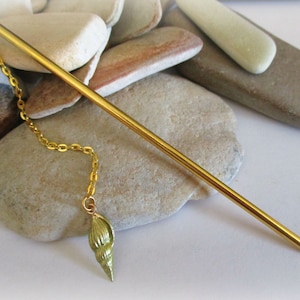 May include: A gold hair stick with a dangling chain and a seashell charm. The stick is about 8 inches long.