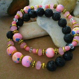 May include: Two bracelets with pink and blue floral beads, black lava rock beads, and gold accents.