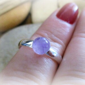 May include: A silver ring with a round, light purple amethyst gemstone.