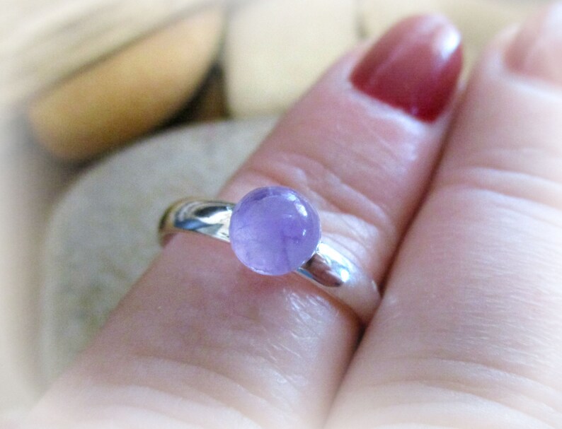 May include: A silver ring with a round, light purple amethyst gemstone.