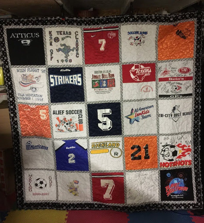 May include: A quilt made of various t-shirts, each with a different design and text. The quilt is made up of 16 squares, with each square containing a different t-shirt. The t-shirts are all different colors and have a variety of designs, including sports teams, school names, and other logos. The quilt is a great way to show off your love of sports and your school spirit.