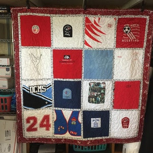 May include: A red, white, and blue patchwork quilt with various patches featuring logos, text, and images. The quilt is made of different fabrics and has a white background with a red border. The patches include logos for a school, a sports team, and a dance studio. The text on the patches includes the words "DCMS", "Allstars", "Bulldogs", and "24".