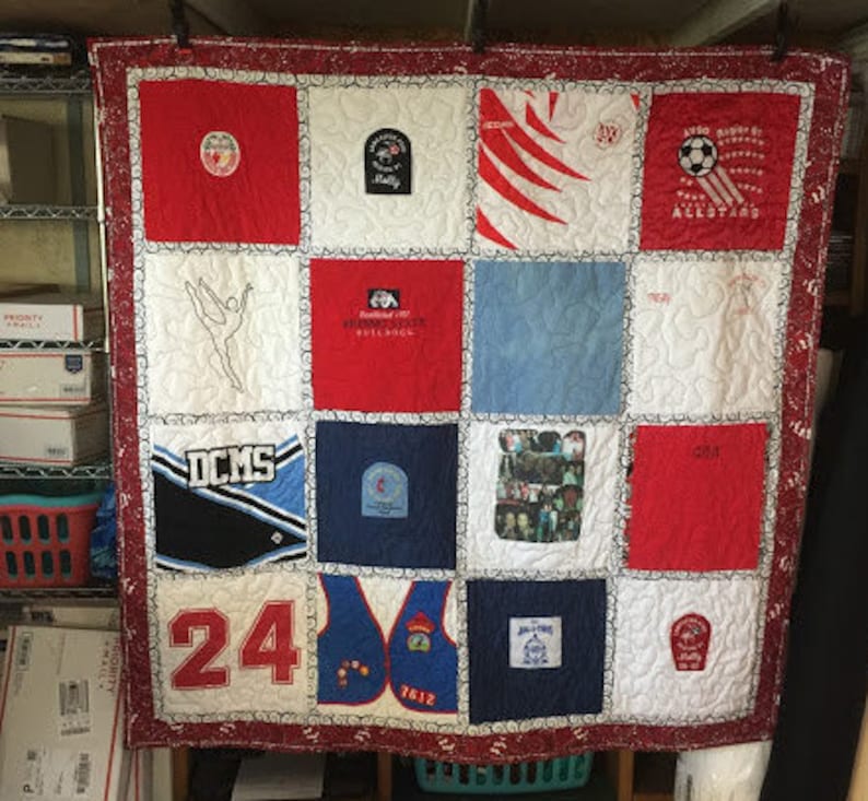 May include: A red, white, and blue patchwork quilt with various patches featuring logos, text, and images. The quilt is made of different fabrics and has a white background with a red border. The patches include logos for a school, a sports team, and a dance studio. The text on the patches includes the words "DCMS", "Allstars", "Bulldogs", and "24".