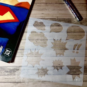 May include: A clear plastic stencil with various shapes for creating comic book speech bubbles and sound effects. The shapes include clouds, stars, and exclamation points.