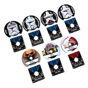 Puede incluir: Un conjunto de fichas y cartas de personajes del juego Star Wars. Las fichas son circulares con retratos de personajes y nombres como "Plo Koon" y "Ric Olie". Las cartas son rectangulares con nombres e información del juego.