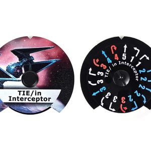 Puede incluir: Dos piezas de juego circulares. Una presenta un caza estelar TIE/in Interceptor contra un fondo espacial. La otra es un dial negro con marcas blancas, rojas y azules, incluyendo números y flechas. El texto "TIE/in Interceptor" es visible.