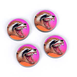 May include: Four round, colorful tokens featuring a cartoon raccoon with a pink and orange background. The raccoon has a fierce expression with its mouth open and teeth showing.