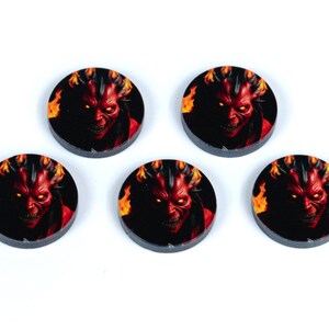 May include: Five round black and red tokens with a red devil face image. The devil has horns and is surrounded by flames.