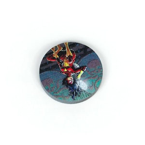 May include: A round, colorful button with a comic book image of a superhero in a red and yellow costume. The superhero is hanging upside down from a web.
