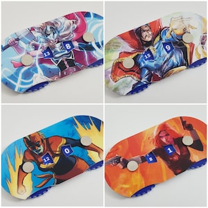 Può includere: Quattro pedine da gioco colorate con diversi personaggi Marvel. Ogni pedina ha un dado blu con un numero su di esso. I personaggi sono Thor, Doctor Strange, Captain Marvel e Black Widow.