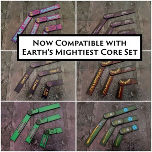 Può includere: Set di strisce di nomi di personaggi in plastica, flessibili, stampate e colorate per un gioco da tavolo. Le strisce sono etichettate con nomi come "Star Lord", "Gamora", "Groot", "White Wolf" e "Killmonger". Il testo "NOW COMPATIBLE WITH EARTH'S MIGHTIEST CORE SET" è visualizzato al centro dell'immagine.
