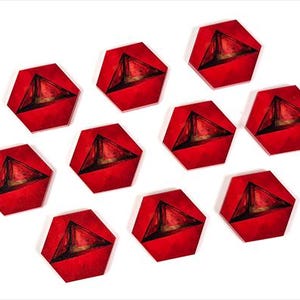Op de afbeelding: Tien rode, zeshoekige spelstukken met een driehoekig ontwerp in het midden zijn gerangschikt op een witte achtergrond. De spelstukken hebben een donker, getextureerd interieur, wat een contrast creëert met de felrode buitenkant.