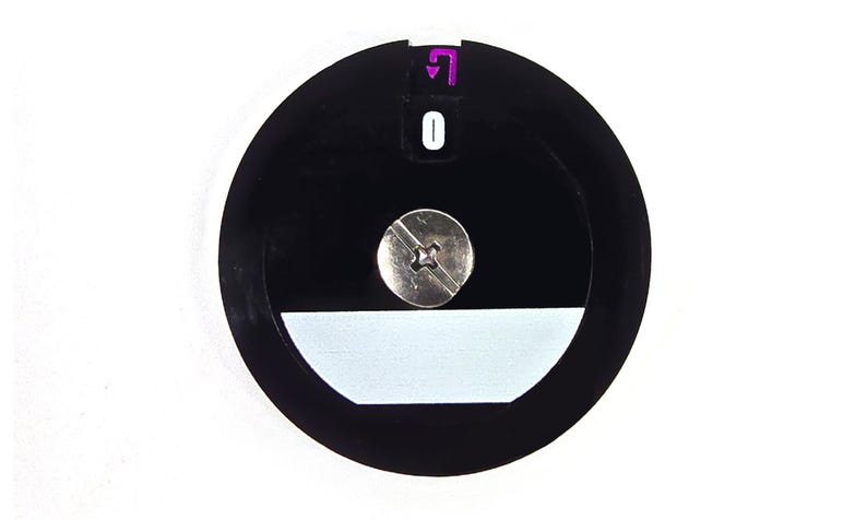 Puede incluir: Un objeto circular negro con un tornillo plateado en el centro. Una forma rectangular blanca en la parte inferior y una flecha morada y el n&uacute;mero 0 en la parte superior. El objeto est&aacute; sobre un fondo blanco.