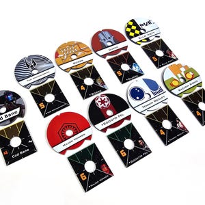 Könnte beinhalten: Eine Sammlung von Spielmarken zum Thema Star Wars. Jede Marke zeigt ein Charakterbild und einen Namen mit einer entsprechenden Nummer. Die Marken sind rund mit quadratischer Basis, vor weißem Hintergrund.