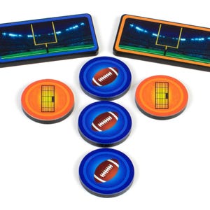 Puede incluir: Un conjunto de fichas para un juego de mesa con temática de fútbol americano. Las fichas son redondas y presentan imágenes de balones de fútbol, zonas de anotación y postes de portería. Las fichas son azules, naranjas y blancas.