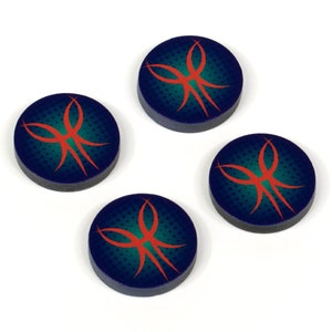 May include: Four round game tokens with a dark blue background and a teal dotted pattern. Each token features a stylized orange design. The tokens are arranged on a white surface.