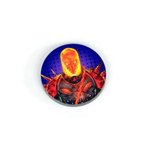May include: A round, blue and purple token with a fiery orange and yellow image of Ghost Rider, a Marvel Comics superhero.