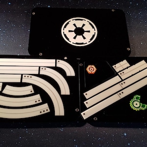May include: Three black acrylic game organizers with white inserts. The top organizer has the Imperial symbol from Star Wars. The middle organizer has curved and straight inserts. The bottom organizer has straight inserts and four red and orange tokens.