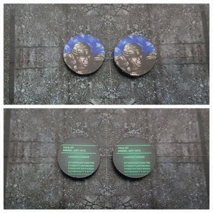 May include: Two black and white circular stickers with the text "V3.47 MODEL ART-47X LAUNCH CODES" and a series of letters and numbers. The stickers are on a gray textured surface.